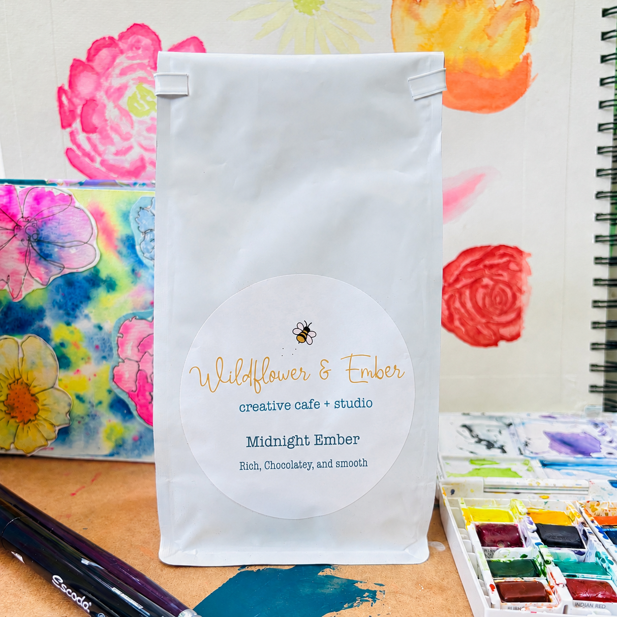 White coffee bag with 'Wildflower & Ember' branding on a colorful floral background
