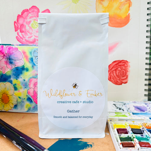 White package with 'Wildflower & Ember' branding on a table with art supplies and floral background